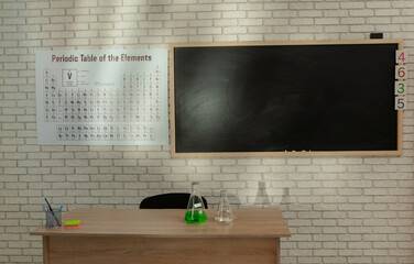 Empty elementary school chemistry classroom with chalkboard, workspace for studying. Shot of teacher's desk with glass bottle, periodic table on the wall.