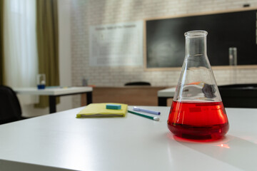 Empty school chemistry classroom with desks, chairs and chalkboard, workspace for teaching and studying. Glass bottle with red liquid on table, close view.