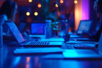 Office workers using laptops in a dark meeting room illuminated by blue and purple neon lights