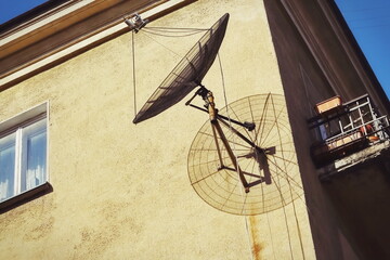 A round satellite dish casting a nice shadow on the corner of a building against a yellow building...