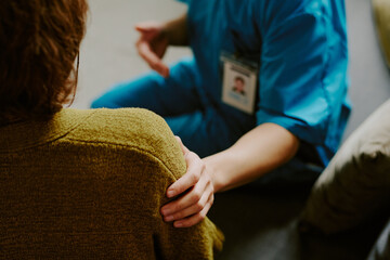 Healthcare professional in blue uniform comforting patient by holding hand, creating a scene of...