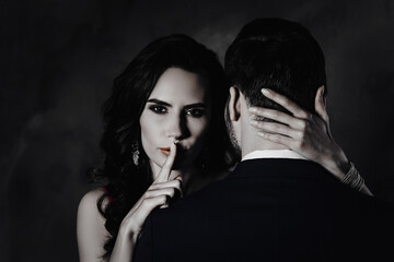 Portrait of tempting brunette lady showing silence sign with forefinger touching secret mysterious gentlemen with rear view, lovely Mr and Mrs isolated on grey background