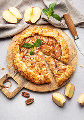 Delicious homemade apple galette with almond flakes and fresh mint on rustic wooden board