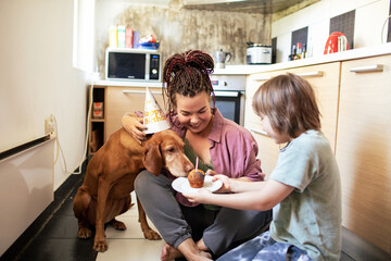 Family celebrating dog's birthday with cupcake and party hat in the kitchen