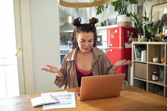 Young woman working from home on laptop with notes and paperwork