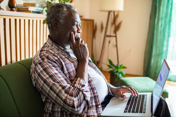 Senior man working on laptop at home in cozy living room
