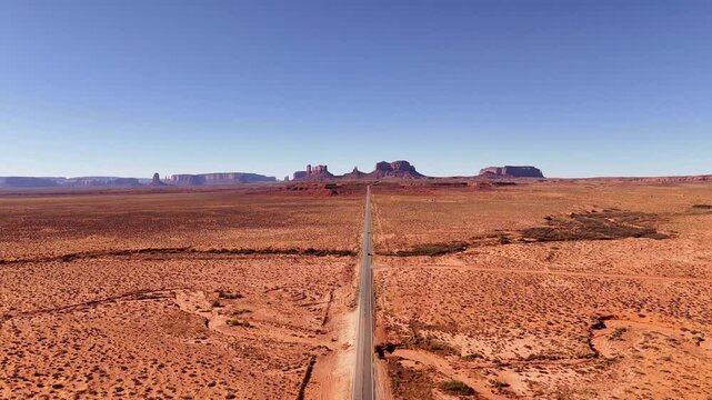 Aerial descending view from Forrest Gump point on route 163 near Monument Valley and Mexican Hat, utah. Bright blue sky. Mesa skyline with the famous mittens in the distance. Cars driving by