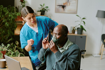 Healthcare professional assisting black elderly man with oxygen mask, scene showing interaction and care in well-lit room with plants and medical equipment
