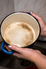 A person holds a blue pot with discolored, burnt stains inside over a sink, ready for cleaning. This image captures the common household task of dealing with burnt cookware
