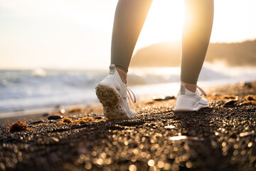 A woman's legs and sneakers on the stone beach at the golden sunset. Female legs in walking motion. Girl's footsteps. Physical activity for fitness and wellness, running through natural landscapes.