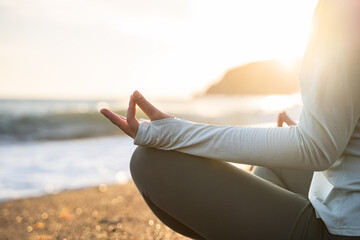 Young woman doing yoga meditation. Side view of a yogi practicing yoga and meditation on the sea beach. Asana Padmasana. Dhyana mudra gesture. Mindfulness. Self care. Healthy mindset. Close up detail.