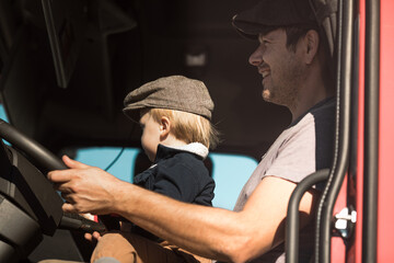A Cute little boy driving is fathers truck with Dad