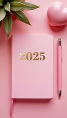 diary notebook pink 2025 gold letters, ballpoint pen. There is a bouquet of roses on the pink table in the left corner