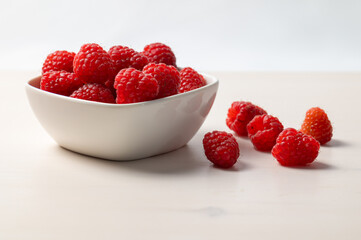 Ripe raspberries in a white bowl, on a red napkin. Raspberry cultivation and use.