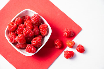 Ripe raspberries in a white bowl, on a red napkin. Raspberry cultivation and use.