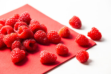 Ripe raspberries in a white bowl, on a red napkin. Raspberry cultivation and use.