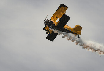 A biplane in the sky at an air show, leaving a smoke trail behind. Close up view from below. © Skatty
