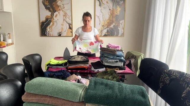 Mulher trabalha passando e dobrando roupas 