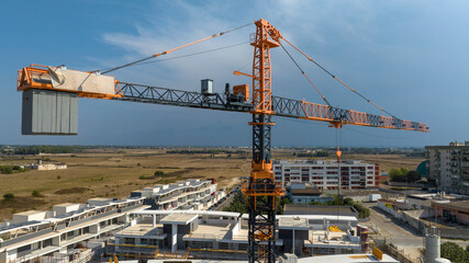 Aerial view of a orange industrial tower crane operating in a building construction site. These large machines allow the concrete plates weight balance. City development concept.