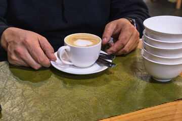 A person holding a white cup of cappuccino with latte art