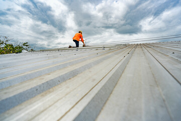 Technician in safety uniform and helmet kneeling on a rooftop, using a drill for precise installation work. A scene highlighting safety, professionalism, and technical expertise in construction.