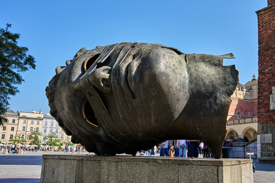 Gigantic bronze head on main market square in Krakow, Poland with Cloth hall in background. Eros Bendato (Eros Bound) Sculpture in Poland
