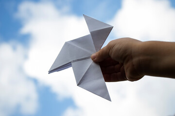 A girl's hand holds a white paper bow tie against the sky as a symbol of Peace.