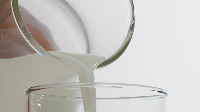 Milk pouring in glass cup close-up. Glass with yogurt, dairy products concept. Drinking fresh lactose-free milk in morning.