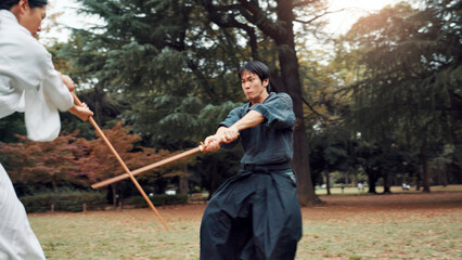 Sword, martial arts and men in outdoor fight together for aikido training, coaching or samurai challenge in park. Weapon, warrior and Japanese people sparring in nature for traditional bokken battle.