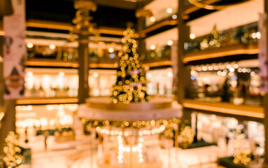 Abstract blurred festive indoor scene with large illuminated Christmas tree with decorations and bokeh lights background in shopping mall