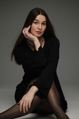 Elegant woman in black dress with long hair poses gracefully on a neutral background