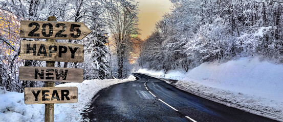 2025 HAPPY NEW YEAR written on wooden sign with arrow pointing to a road crossing a snowy forest in alpine mountain