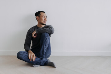 Happy creative freelance Asian man sitting on the floor smile and looking out.