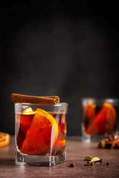 Homemade traditional winter red mulled wine drink or grog cocktail made with slices of orange citrus fruit decorated with cinnamon stick served in glass on brown table on black wall with copy space