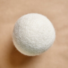Minimalist close-up of a wool dryer ball on a beige background, emphasizing texture and natural fibers, suitable for eco-friendly laundry themes