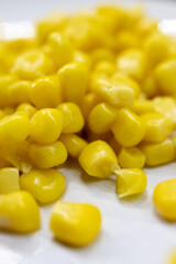 macro view of bright yellow sweet corn kernels on a white plate, focusing on texture, freshness, and natural appeal