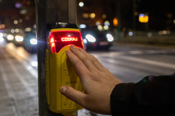 man pressing illuminated pedestrian crossing button at night, red glowing 