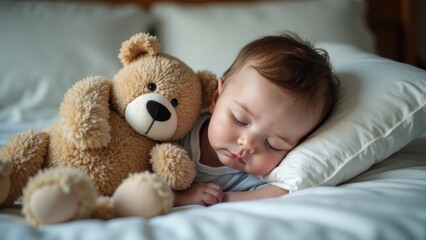 A baby lies peacefully asleep on a white bed, resting their head on a soft pillow next to a fuzzy teddy bear. The warm, cozy atmosphere creates a serene setting