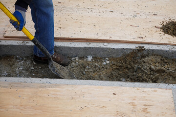 Leg of laborer with shovel digging a ditch through a channel between concrete slabs