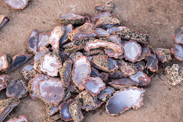 Pile of polished agate stones with varying colors and patterns on sandy surface