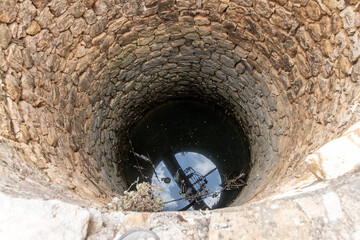 Round stone well with water reflecting sky and fallen branches