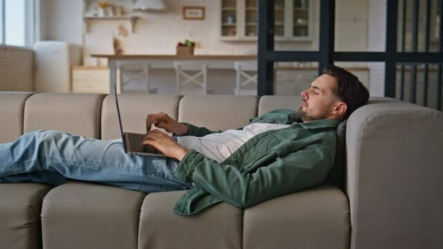 Man working laptop lying comfortable at home couch. Busy guy freelancer work