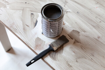 Opened grey paint and brush on top of the edge of old table. Renovation DIY