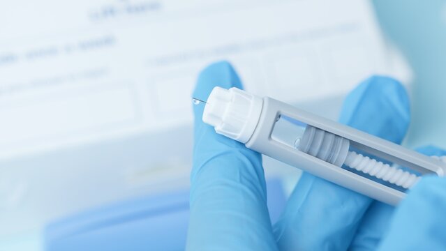 Close up on a needle on diabetic medication pen. Hands with blue glowes taping pen. High quality photo