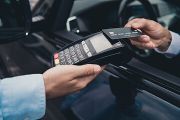 Businessman making contactless payment with card on wireless terminal by parked car outside on city...