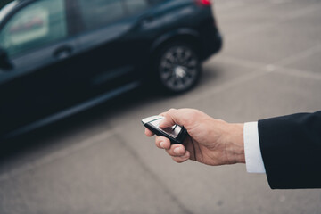 Elegant businessman in parking lot unlocking his car with remote key, reflecting modern travel and business lifestyle