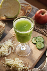 A glass cup of fresh green cabbage and cucumber juice with red apples