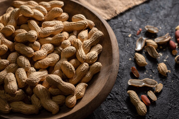 Primer Plano de cacahuetes con cáscara en un plato de madera sobre mesa vintage, ideal para conceptos de alimentación saludable y natural.