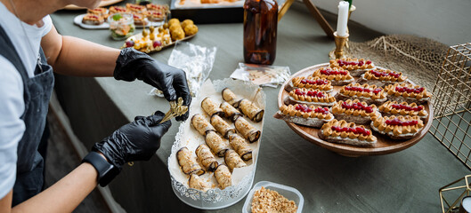 A person who is wearing black gloves is carefully and meticulously preparing food on a table, ensuring that all ingredients are properly handled, organized, and ready for the upcoming meal