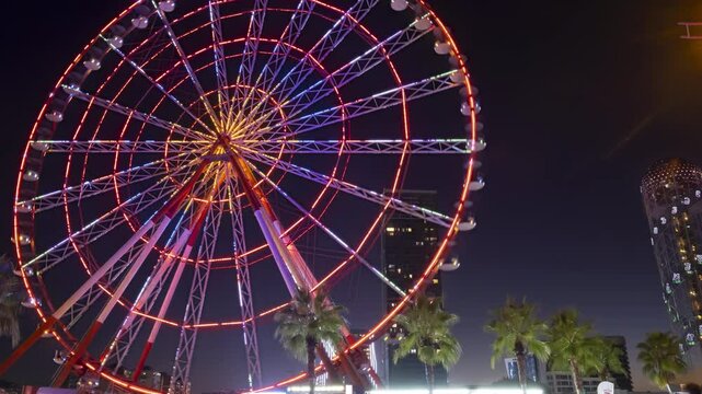 Timelapse of moving illuminated Ferris wheel on embankment in Batumi evening.